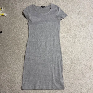 Grå kortärmad klänning från Primark strl 36 - En enkel och stilren grå klänning från Primark. Modellen är rak och kroppsnära med korta ärmar och rund halsringning. Perfekt basplagg som funkar till många olika looks.