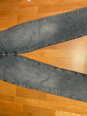 Blå jeans från Woodbird, loose längd 32 midjan 27 - Säljer ett par klassiska blå jeans från Woodbird med rak passform och snyggt slitna detaljer. Jeansen har fem fickor, orange kontrastsömmar och en brun patch bak i midjan. Perfekta till vardagslooken och funkar året runt.