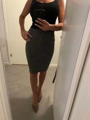 Grå ribbad pennkjol i stickat material - Säljer en grå, ribbad pennkjol i stickat material. Kjolen är figurnära och går till knäna, perfekt för dig som gillar en slim och stilren look. Den har en enkel design utan detaljer och passar snyggt till både sneakers och klackar.