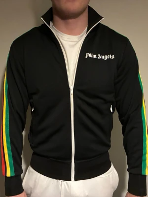 Palm Angels svart zip hoodie S - Säljer min Palm Angels svart hoodie med dragkedja och vita detaljer. Ärmarna har färgglada ränder i grönt, gult och rött. Logga på bröstet. Knappast andvänd pågrund av att den blivit för liten för mig. Självklart äkta och väldigt bra skick! Nypris 4000