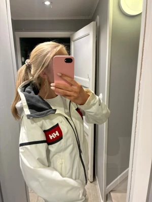 Vit vindjacka från Helly Hansen - Säljer en vit jacka från Helly Hansen med svarta och röda detaljer!! Sååå fin och även väldigt bra skick!