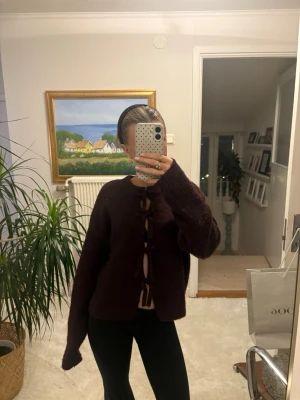 Vinröd kofta med rosettknäppning - Supermysig vinröd kofta med lång ärm och snygga rosettknäppningar framtill. Koftan är stickad och har en loose fit, perfekt att slänga på sig när det är kyligt ute. Storlek 158/164