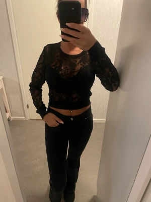 Svart blommig spetsblus - Säljer en svart blus från H&M i transparent spets med blommigt mönster. Modellen är croppad och har långa ärmar samt ribbade muddar vid ärmslut och nederkant. Perfekt för dig som gillar en edgy och trendig stil.