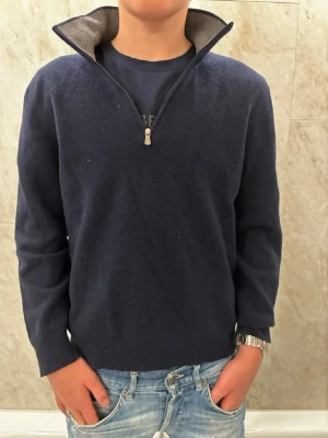 Mörkblå stickad tröja med half zip - Mörkblå stickad tröja med hög krage och half zip-dragkedja. Tröjan har lång ärm och en klassisk. Tröjan är 100% Cashmir och perfekt för lite kallare dagar. Hör av er vid frågor!