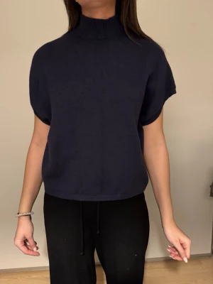 Mörkblå stickad topp från Kappahl - Säljer en mörkblå stickad topp från Kappahl i storlek M. Modellen har hög krage, korta ärmar och en loose passform. Perfekt att styla med både jeans och kjol för en chill look.