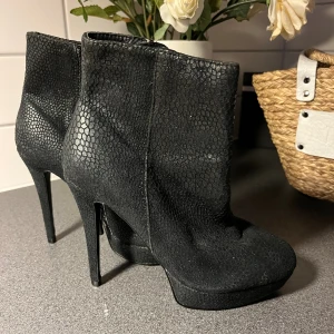 Svarta stövletter med platå och klack - Säljer ett par svarta stövletter med höga klackar(12cm) och platåsula. Skorna har ett coolt ormskinnsmönster och dragkedja på sidan för enkel påtagning. Materialet ser ut som syntet med struktur och de har en spetsig siluett som ger en edgy vibe .I använt gott skick! Små i storleken!!