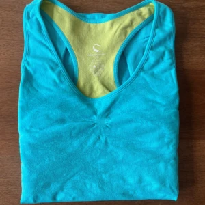 Träningstopp blå från märket climawear - Säljer ett fräscht och bekvämt träningslinne i en härlig turkos/blå färg. Perfekt för gym, löpning, dans, yoga eller vardagsaktiviteter! Materialet är mjukt, stretchigt och sitter snyggt utan att kännas tight. Racerback-designen ger full rörelsefrihet och håller sig bekväm även vid intensiva pass.  Storlek: L  Sitter superbra och formar sig efter kroppen Svalt och snabbtorkande material  