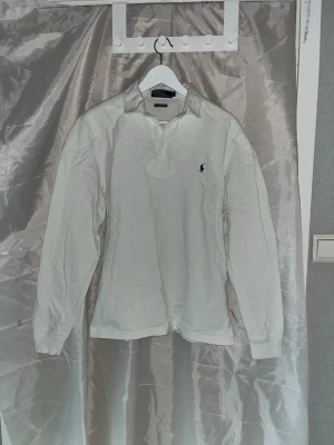 Ralph Lauren tröja  - Vit långärmad pikétröja från Polo Ralph Lauren i bomull. Klassisk krage, knappar vid halsen och förstärkt matrial på axlar och armbågar. Axelbredd 46cm, längd 66cm, armlängd 62cm.  Ifall det inte finns någon bild i annonsen där jag bär plaggen jag säljer så är det för att jag ej kan ha storleken heller passformen, så kolla måtten för storlek och googla på modellnamnet för passform 😉 1,20