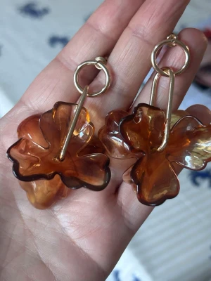 Bruna blomformade örhängen - Unika örhängen i transparent brun plast med blomformade hängen och guldfärgade detaljer. De har en cool och lekfull design som verkligen sticker ut. Perfekta för dig som gillar att addera lite färg och form till din stil.