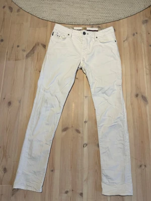 Vita raka jeans från Tramarossa  - Snygga vita jeans från Tramarossa med slimmad passform och klassisk femficksdesign. Jeansen har bälteshällor, knappgylf och diskreta detaljer. Perfekta för en clean och fräsch look. Materialet känns mjukt och följsamt. Skicket på jeansen är mycket bra och det är bara en av lapparna som har lossnat på två ställen men det går enkelt att fixa!