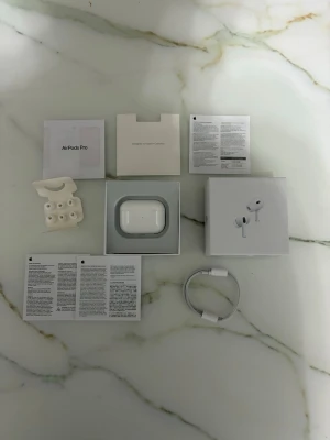Apple AirPods Pro 2 - Säljer ett par vita Apple AirPods Pro med trådlöst laddningsetui. Hörlurarna har silikonproppar i olika storlekar, brusreducering och levereras med originalkartong, laddkabel och manualer. Perfekta för musik, samtal och träning.