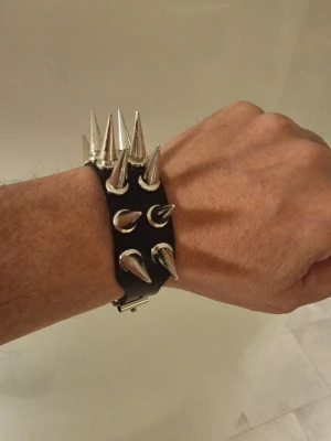 Armband punk med spikar - Armband punk med spikar. Europeisk och Amerikansk punkstil. 2-rads spikförsedd fauxläderarmband. Längd 25,8 cm. Bredd 2,6 cm.