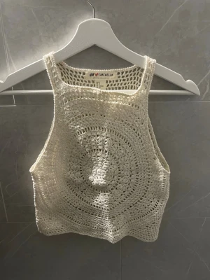 Vit virkad linnetopp från H&M Coachella - Säljer en vit virkad linnetopp från H&M Coachella-kollektionen. Toppen är ärmlös och har ett snyggt cirkulärt mönster framtill. Perfekt för sommarens festivaler och strandhäng. Storlek S men sitter som XS