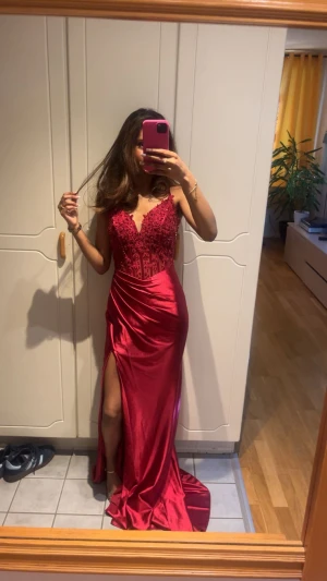 Röd balklänning med spets och slits - Säljer en superfin röd balklänning med glittrig spets upptill och transparent detaljerad mesh. Klänningen har smala axelband, öppen rygg med snörning och en slits framtill. Kjolen är i glansigt satinmaterial och passar perfekt för bal eller bröllop. Endast använd 1 gång❤️För mer information kontakta privat!