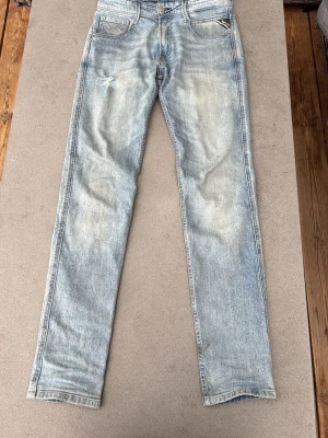 Ljusblå jeans från Replay - Säljer ett par ljusblå jeans från Replay anbass med en klassisk femficksdesign och slitningar på vänster lår. Jeansen har raka ben och en snygg tvättad look med Replay-märke på bakfickan. Perfekt för dig som gillar en avslappnad stil. Storlek 27/30 