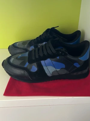 Valentino rockrunners - Snygga sneakers från Valentino med blått och svart kamouflagemönster. Skorna har svarta detaljer, svarta skosnören och en robust svart sula. Materialet är en mix av läder och textil vilket ger en cool och modern look. Dustbag ingår
