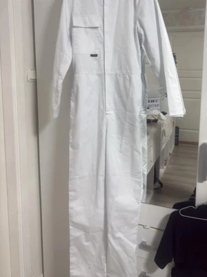 Helt ny studentoverall  - Studentoverall med långa ärmar och rak passform. Knappar framtill och en bröstficka med lock. Resår i ryggen för bättre passform. Helt ny med prislapp, säljer pga för liten storlek