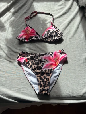 Leopardmönstrad bikini med rosa blommor - Snygg bikini med leopardmönster och stora rosa blommor. Överdelen har trekantsform och justerbara band, medan underdelen är klassisk med hög midja. Perfekt för sommarens strandhäng och poolpartyn. Materialet är syntet och torkar snabbt. Överdelen var lite stor på mig med 70A i storlek annars💕 Har aldrig använt och tvättar den innan den ska skickas🥰