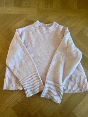 Ljusrosa stickad tröja Gina Tricot - Mysig ljusrosa stickad tröja från Gina Tricot med ribbade muddar vid ärmslut och nederkant. Tröjan har en rak passform, rund halsringning och är tillverkad i ett mjukt material som passar perfekt för kyligare dagar.