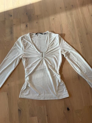  långärmad topp med silverdetalj framtill - Snygg vit långärmad topp med smickrande silver detalj framtill och lätt urringning. Mjuk och stretchig i materialet, sitter fint på kroppen. Perfekt både till vardags och fest! Bra skick, sparsamt använd.