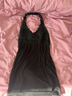Svart spetsklänning med halterneck - Snygg svart kortklänning med halterneck och spetsdetaljer upptill. Från ginatricot i storlek S