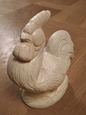 Vit tupp i keramik - Dekorativ tupp i vit keramik med detaljerat mönster som framhäver fjädrarna. Perfekt som prydnad till hemmet eller som samlarobjekt. Tuppen har en klassisk form och står stadigt på en oval bas.