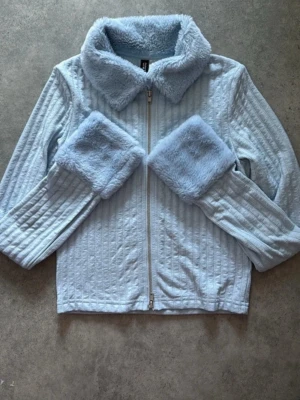 Ljusblå teddyjacka från Divided - Supermjuk ljusblå teddyjacka från Divided med fluffig krage och muddar. Jackan har dragkedja framtill och ett quiltat mönster i tyget. Perfekt för dig som vill ha en mysig och trendig look med extra fluffiga detaljer.