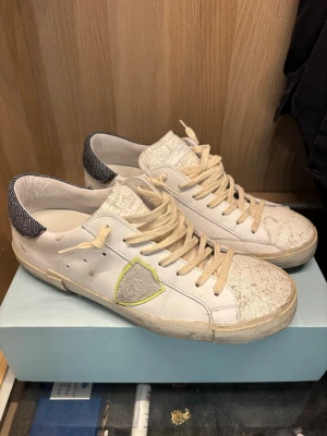 Philippe Model sneakers - Snygga vita sneakers från Philippe Model med beige snörning och sprucken effekt på tån och plösen. Skorna har använts bara ett par gånger. Mycket bra skick! Box och dustbag ingår.