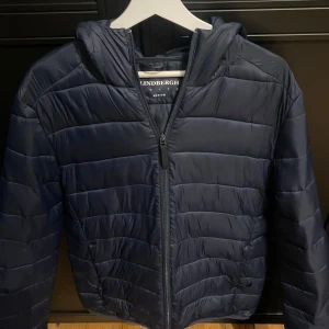 Lindbergh Jacka  - Säljer en snygg dun jacka perfekt till hösten/vintern. Har använt den en vinter. Den är i väldigt bra skick och har inte några defekter. Köpte den för 1200.           Litet hål vid fickan inget man tänker på