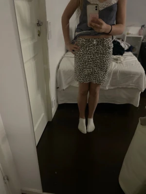 Leopardmönstrad kortkjol i vitt och grått - Säljer en snygg kortkjol med leopardmönster i vitt och grått. Kjolen har en rak passform och är perfekt för dig som vill sticka ut lite extra. Den är tillverkad i ett mjukt material och har en bekväm midja. Har aldrig använts