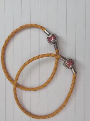 Två gula armband - Säljer två armband i flätat gult läder med ett metallspänne där det står 'hej' i rött. Säljer båda för 40 kr, annars en för 20 kr. Notera att de är ganska små i storleken.