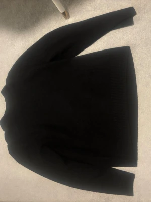 Svart stickad tröja med rund hals - En klassisk svart stickad tröja med rund hals och ribbade muddar vid ärmslut och nederkant. Perfekt för lager-på-lager och enkel att matcha med olika outfits. Materialet ser mjukt och bekvämt ut.