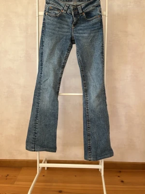Blå bootcut jeans från Gina tricot - Säljer ett par klassiska blå bootcut jeans från Gina tricot. Jeansen har fyra fickor, knappgylf och snygga detaljer på bakfickorna med silverfärgade knappar. Tillverkade i slitstark denim med lätt tvättad look och låg midja.