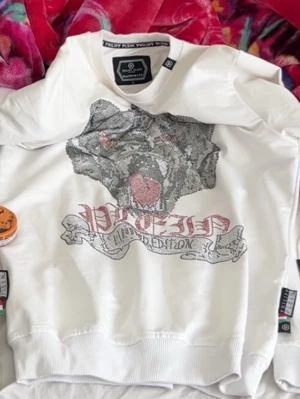 Vit hoodie från Philipp Plein - Cool vit hoodie från Philipp Plein med stort glittrigt hundmotiv och texten 'Plein Limited Edition' på framsidan. Hoodien har ribbade muddar och en klassisk passform. Perfekt för dig som vill sticka ut med en unik design.