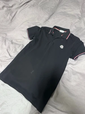 Svart Moncler pikétröja  - En riktigt snygg svart moncler piké, perfekt till sommaren! Storlek XL, passar L/M. Några små fläckar som nog går bort i tvätten. Hör av er vid frågor/prisförslag! ✌️