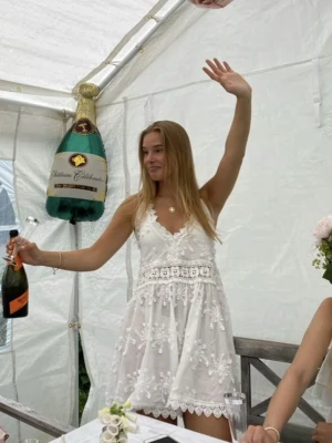 By Malina klänning strl XS  - Söt vit klänning med tunna axelband, v-ringning och detaljerad spets samt broderade blommor. Klänningen har en markerad midja med spetsband och en lätt utsvängd kjol. Perfekt för sommarens alla tillfällen.