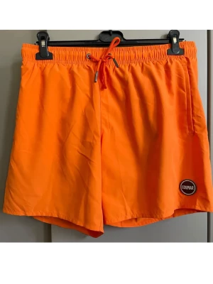 Orange badbyxor från Colmar - Snygga orange badbyxor från Colmar med elastisk midja och dragsko för perfekt passform. Klassisk modell med sidofickor och Colmar-logga på vänster ben. Tillverkade i snabbtorkande material, perfekta för stranden eller poolen.