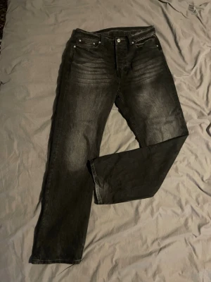 Svarta jeans från weekday - Säljer ett par svarta jeans från weekday med diskreta slitningar och klassisk femficksdesign. Jeansen har raka ben och är tillverkade i denim med en snygg tvättad look. Perfekta för dig som gillar en stilren och avslappnad vibe.
