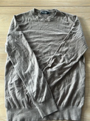 Brun stickad tröja från Dressmann - En enkel och stilren brun stickad tröja från Dressmann. Tröjan har rund halsringning, långa ärmar och ribbade muddar vid ärmslut och nederkant. Perfekt för lager på lager och passar till det mesta.