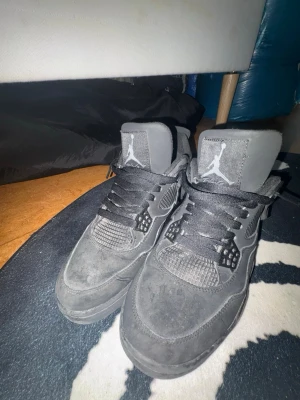 Black cat Air Jordan 4 Retro sneakers - Säljer ett par svarta Air Jordan 4 Retro sneakers med klassisk Jumpman-logga på plösen. Skorna har en cool meshdetalj på sidorna, svarta skosnören och är tillverkade i mocka och textil. Perfekta för dig som gillar streetwear och sportig stil. Kan tvätta och kommer med Crep protect