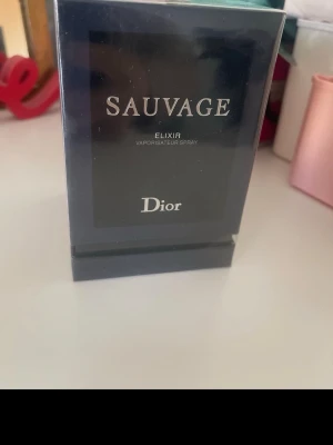 Dior Sauvage Elixir parfym - Dior Sauvage Elixir är en exklusiv parfym i en elegant mörkblå glasflaska med silverfärgad text. Flaskan har en stilren och lyxig design som verkligen sticker ut på hyllan. Perfekt för dig som gillar kraftfulla och unika dofter.