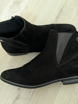Svarta Chelsea boots från s.Oliver - Stilrena svarta Chelsea boots från s.Oliver i mocka med elastiska sidopaneler och låg klack. Klassisk siluett med diskret logga på hälen och bekväm passform. Perfekta för dig som gillar en tidlös och snygg look.