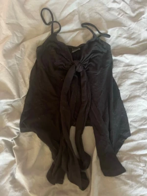 Svart linnetopp från Gina Tricot - Säljer en svart linnetopp från Gina Tricot med smala axelband och knyt framtill. Toppen har en croppad passform och är perfekt för varma dagar. Enkel och stilren design som passar till mycket.