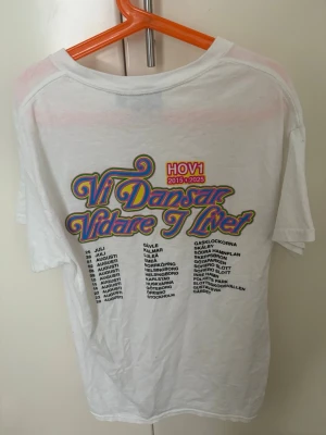 Vit Hov1 t-shirt med tryck från 2025 - Vit t-shirt från Hov1 med färgglatt turnétryck på ryggen och liten krona broderad på bröstet. Klassisk rund hals och korta ärmar, skriv priser vill veta hur mycket jag kan få den för💞