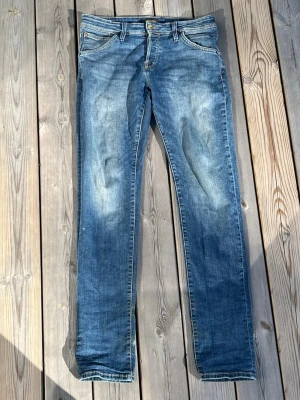 Jack & Jones Glenn - Säljer ett par blå slim fit jeans med snygga slitningar och tvättade detaljer. Klassisk femficksmodell med dragkedja och knapp i midjan. Jeansen har en skinnpatch bak i midjan och raka ben. Perfekta till en avslappnad stil. Stl 30/32