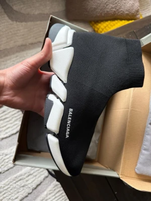 Balenciaga Speed Trainer svarta sneakers - Svarta Balenciaga Speed Trainer sneakers med vit chunky sula och stickad ovandel i stretchigt material. Strump-liknande passform och Balenciaga-logga på sidan. Perfekta för dig som gillar en futuristisk och clean stil.