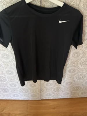 Svart Nike Dri-FIT t-shirt - Svart t-shirt från Nike. Tillverkad i Dri-FIT-material som andas och transporterar bort fukt, perfekt för träning. Kortärmad och med rund halsringning för en sportig look.