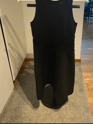 Svart ärmlös klänning med dragkedja - Snygg svart ärmlös klänning med rund halsringning och markerad midja. Klänningen har en cool öppen detalj i ryggen och en synlig dragkedja bak. Perfekt för dig som gillar stilrena och moderna plagg.