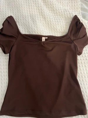 Jättefin brun topp till sommaren från Nelly! 💞 - Snygg brun topp från Nelly med puffärmar och bred, något v-ringad halsringning. Tillverkad i mjuk material som sitter tight och bekvämt. Perfekt att styla med jeans eller kjol för en trendig look. Perfekt till en sen sommarkväll 💞🥂❤️