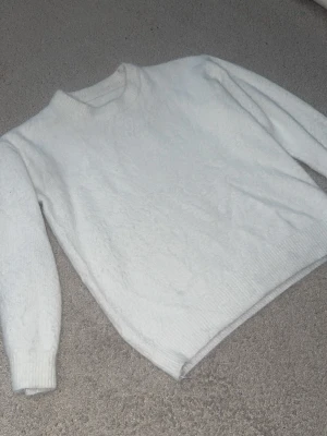 Vit stickad tröja - Mysig vit stickad tröja med rund hals och långa ärmar. Tröjan har ribbstickade muddar vid ärmslut och nederkant. Perfekt för kalla dagar och enkel att matcha med olika outfits.